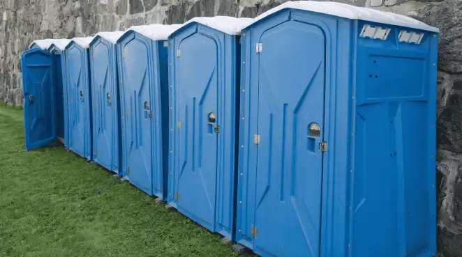 Row of blue portable toilets lined up on grass against a stone wall for event sanitation in Santa Ana, CA