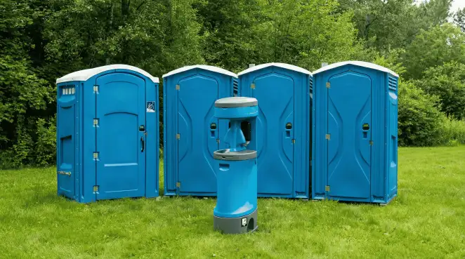 Four blue portable toilets and a matching hand washing station on grass near trees, a common sight at local outdoor events in Santa Ana, CA