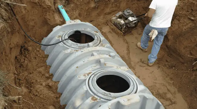 Septic tank installation showing a technician compacting soil around a new poly septic tank in an excavation pit in Santa Ana, CA